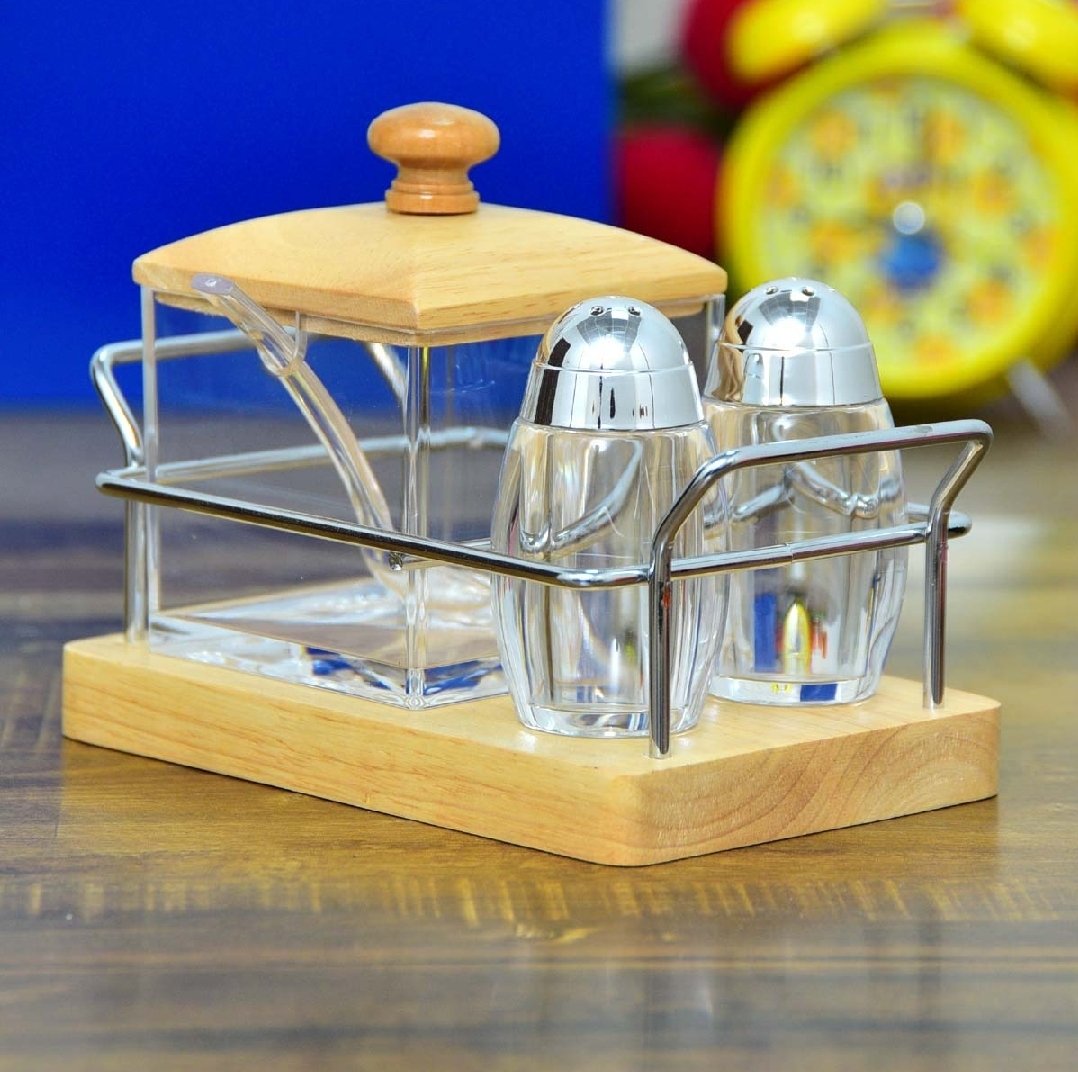 Three-piece glass cruet set with two stainless steel seasoning shakers and a lidded condiment jar on a bamboo base with metal holder.
